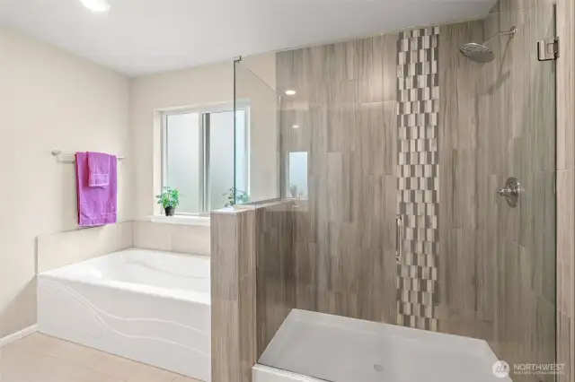 Stylish and serene, this bathroom showcases a custom-tiled walk-in shower with mosaic accents, a deep soaking tub, and a large frosted window that lets in natural light while maintaining privacy.