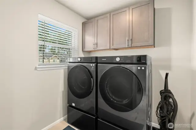 This dedicated laundry room makes chores a breeze with front-load Samsung washer and dryer, upper cabinetry for storage, and a window that brings in natural light.