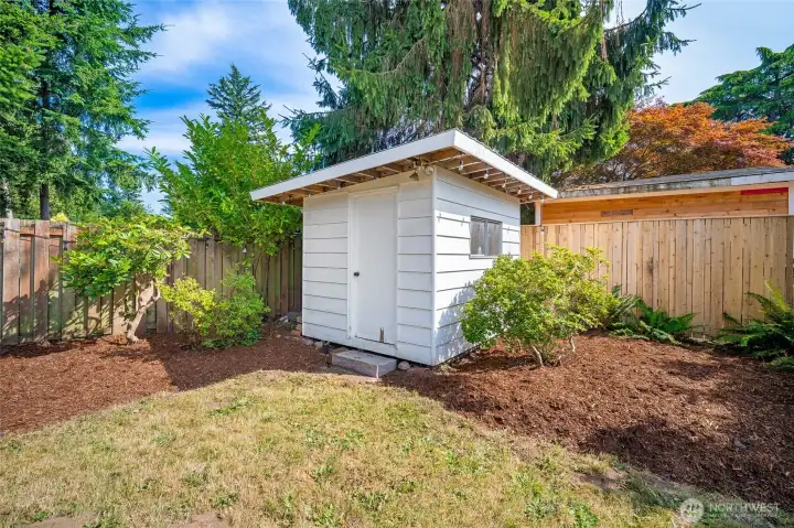 A backyard shed adds extra storage, framed by mature trees and gardens.