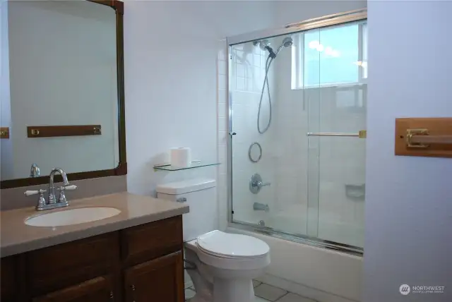 Tiled main bathroom with Corian countertop and shower with sliding glass door.