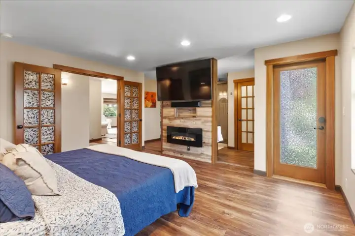 Primary suite featuring an electric fireplace, TV wall, and direct outdoor access with a view toward the ensuite. Primary suite featuring an electric fireplace, TV wall, and direct outdoor access with a view toward the ensuite.