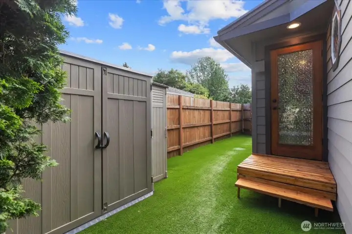 Primary bedroom walk-out to a private side yard featuring a hot tub, garden shed, and low-maintenance artificial turf. Primary bedroom walk-out to a private side yard featuring a hot tub, garden shed, and low-maintenance artificial turf.