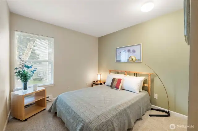 The third bedroom offers a serene setting ideal for restful nights or productive afternoons. With room for a full-sized bed, this space also features a soft accent wall and a large window that frames views of the surrounding greenery, bringing the outdoors in.