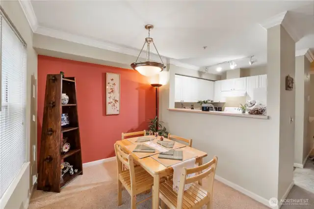 Enjoy meals in a cozy, well-lit dining area that effortlessly connects to the kitchen through a convenient pass-through bar—perfect for casual dining and easy entertaining. A warm accent wall adds character to the space, while crown molding and soft lighting create an inviting and polished feel.