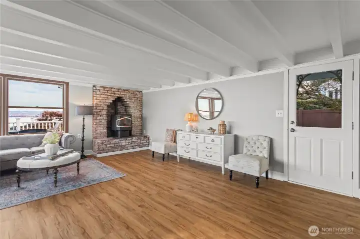 New flooring covers the main level, continuing from room to room, and a pellet stove adds warmth to this spacious living room. Notice the door on the right that leads out to the driveway, lawn, garden shed, and pergola.