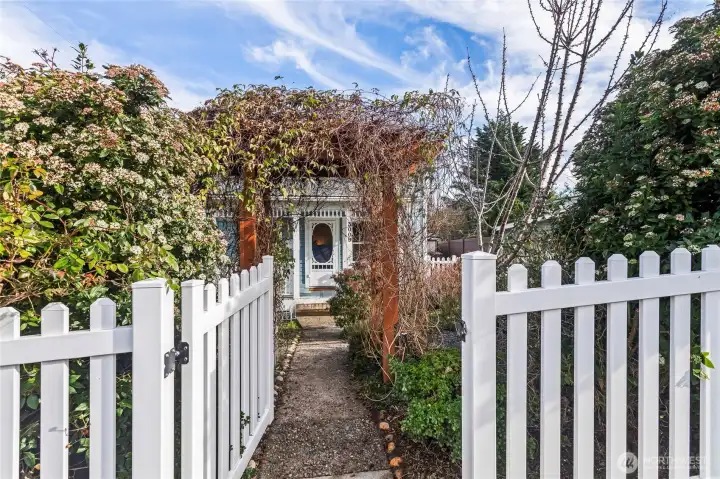 Enclosed by a white picket fence, the garden welcomes you to the home with a vine-covered arbor over the path.