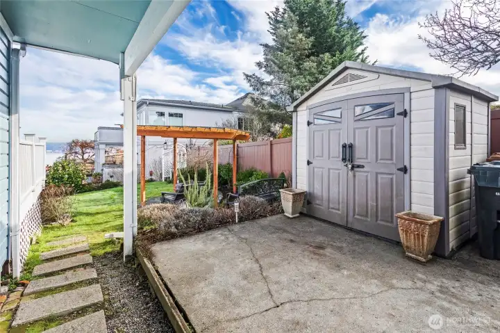 A garden shed and patio are set at the end of the driveway. Stepping stones lead to the lawn and pergola.