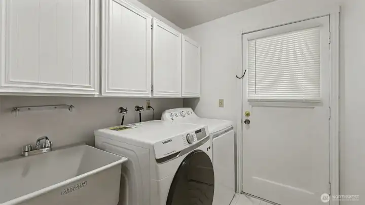This functional laundry space includes upper cabinetry for storage, a utility sink, and easy exterior access.