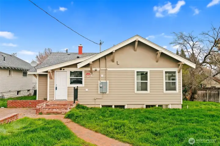 Back of home with spacious backyard and brick patio/walkway.