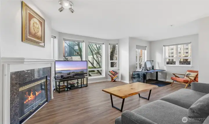 Living room with gas fireplace and floor to ceiling windows. Windows have remote control blinds. Updated LVP flooring.