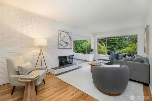 Bright and airy mid-century living room with large west-facing picture windows, original hardwood floors, and a cozy fireplace—perfect for relaxing or entertaining. Enjoy tranquil territorial views and an adjacent bonus space ideal for a home office or reading nook.