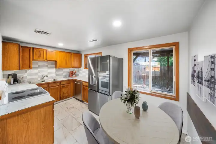 This bright kitchen features warm wood cabinetry, stainless steel appliances, and a dining area with a view of the backyard. *virtually staged*