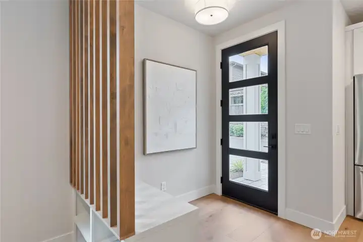 This entryway blends warmth and modernity with a black-panel glass front door that invites natural light, while the slatted wood partition and built-in bench create a functional yet artful transition into the home.