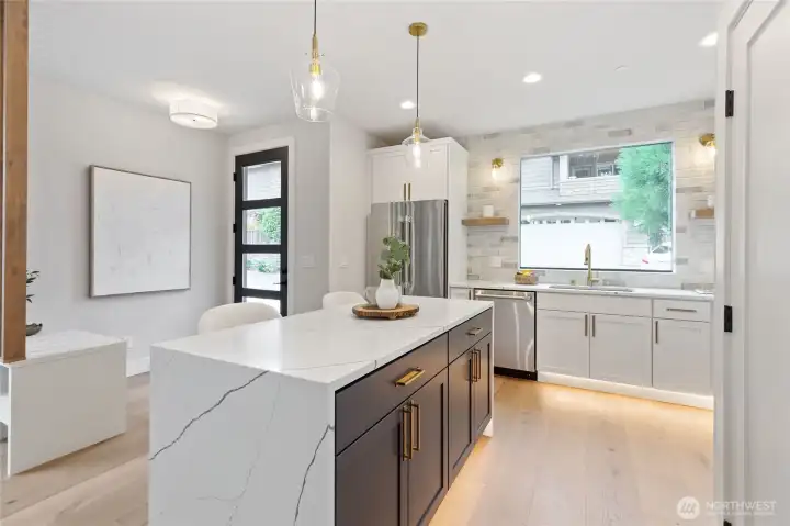 The island anchors the kitchen with its striking white marble surface and rich dark cabinetry, offering both a visual centerpiece and a functional hub for cooking, gathering, and casual dining.