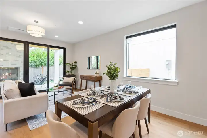 This fluid dining and family room layout blends comfort and sophistication. Natural light pouring in through expansive glass doors that connect seamlessly to the lush outdoor patio with a beautiful fireplace.