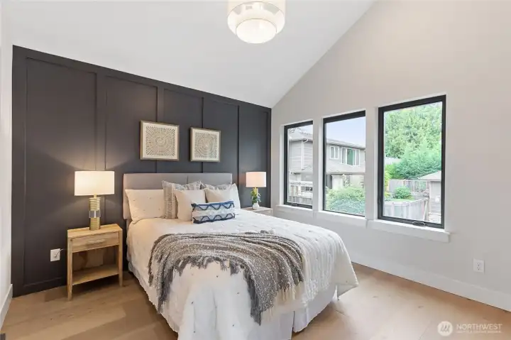 This inviting primary bedroom features a bold charcoal accent wall, layered textures, and abundant natural light—creating a restful retreat with modern elegance.