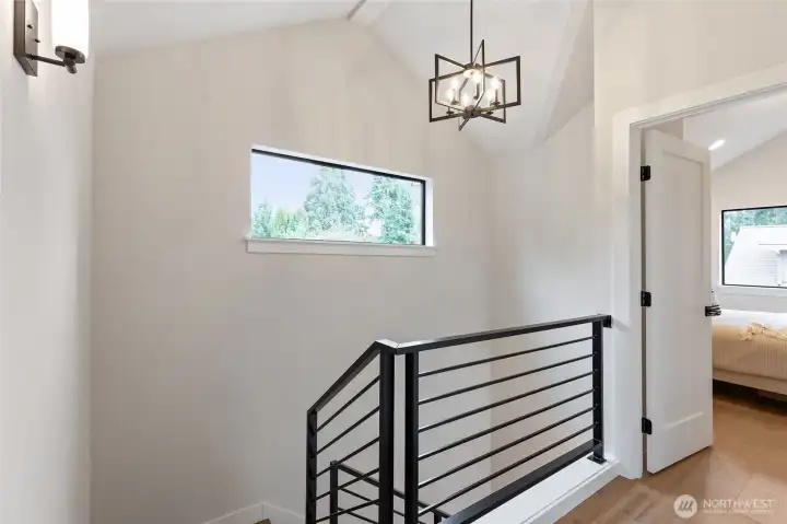 This upper landing blends clean lines and natural light with a sleek metal railing and geometric pendant—offering a quiet transition space with modern character.