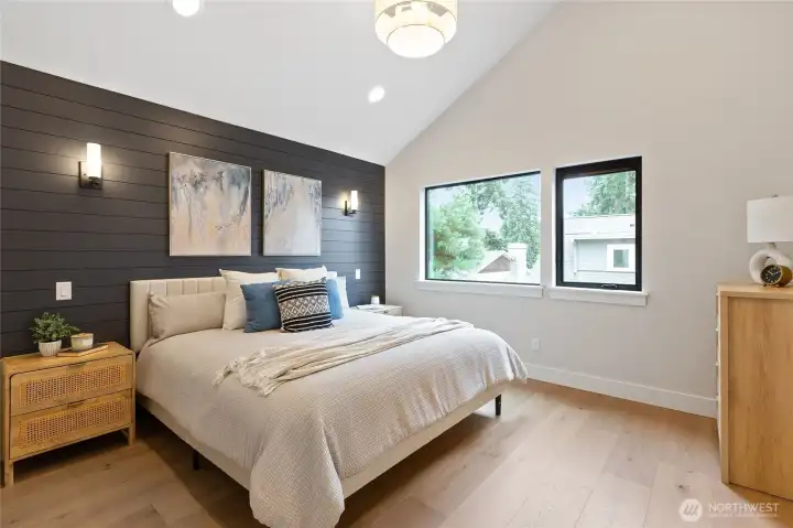 This serene primary bedroom features a dark shiplap accent wall, vaulted ceiling, and soft neutral tones—elevated by natural light and clean, modern styling.