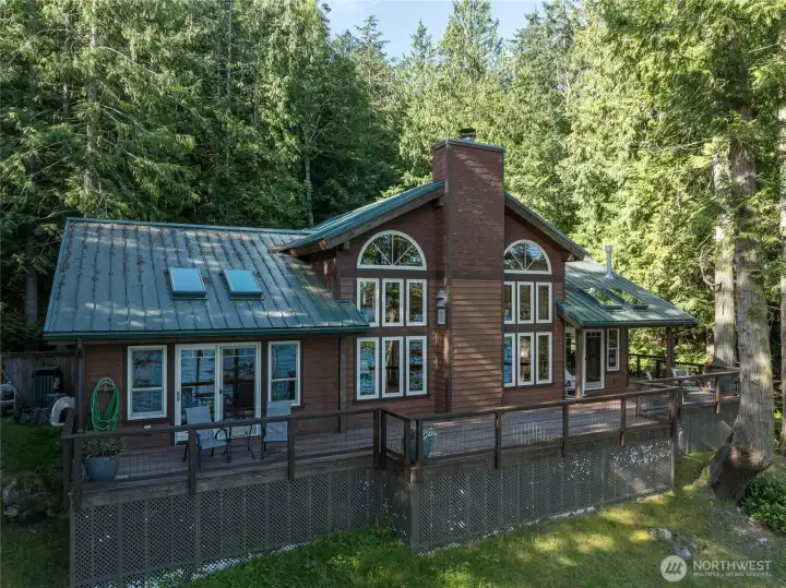 Water side of the home. Access onto wrap around deck is offered from main level primary ensuite and the dining area. Water side of the home. Access onto wrap around deck is offered from main level primary ensuite and the dining area.