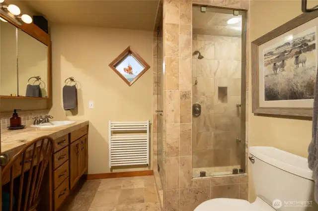 Primary bath spacious shower with Travertine tile with multiple shower heads and steamer. Heated towel rack and vanity.