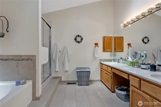Luxurious primary bathroom featuring heated floors, dual sinks with quartz counters, a soaking tub, a separate shower, and direct access to a spacious walk-in closet