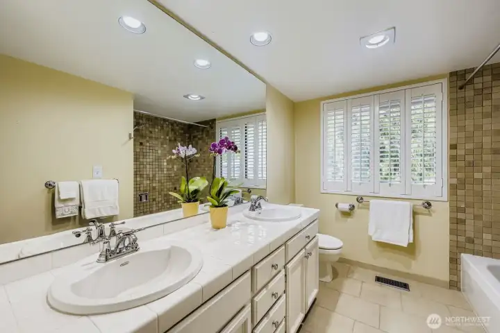 The guest bath boasts a large window with plantation shutter, excellent lighting, dual sinks, abundant cabinetry and tile floors.
