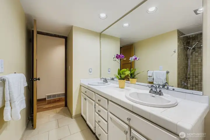 The full guest bath features dual sinks, tile countertops and many drawers and cabinets in the vanity.