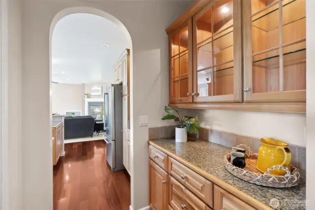 Entertain like a pro with this stunning butler's pantry! Featuring sleek granite countertops, hickory cabinets, and upper glass-front cabinetry that showcases your finest glassware, this space is all about style and function. The arched doorway elegantly connects to the kitchen and family room, making it the perfect spot for mixing cocktails or setting up a buffet. It’s the ultimate blend of sophistication and convenience!