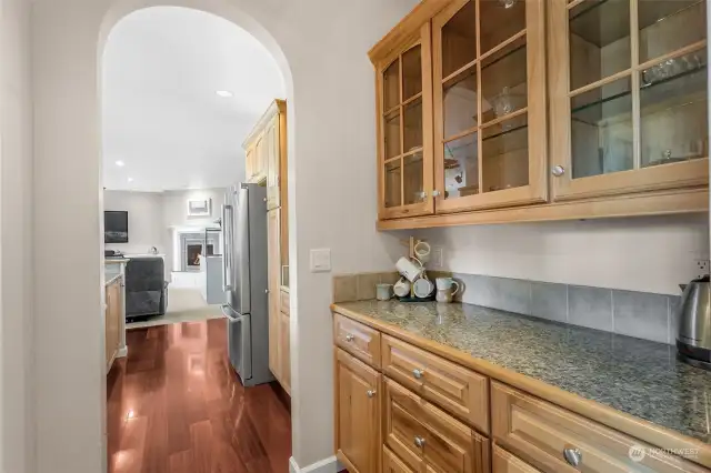 Entertain like a pro with this stunning butler's pantry! Featuring sleek granite countertops, hickory cabinets, and upper glass-front cabinetry that showcases your finest glassware, this space is all about style and function. The arched doorway elegantly connects to the kitchen and family room, making it the perfect spot for mixing cocktails or setting up a buffet. It’s the ultimate blend of sophistication and convenience!