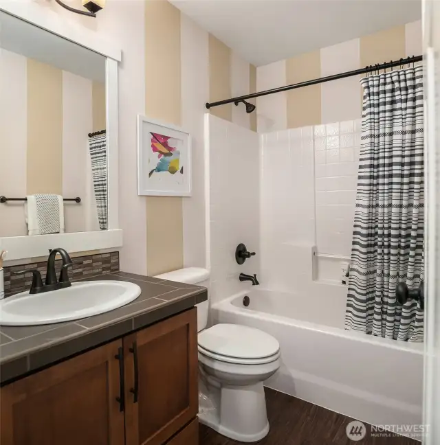 This lower level full guest bath includes an elegant tile and backsplash vanity with warm wood cabinets and easy storage with soaking tub.