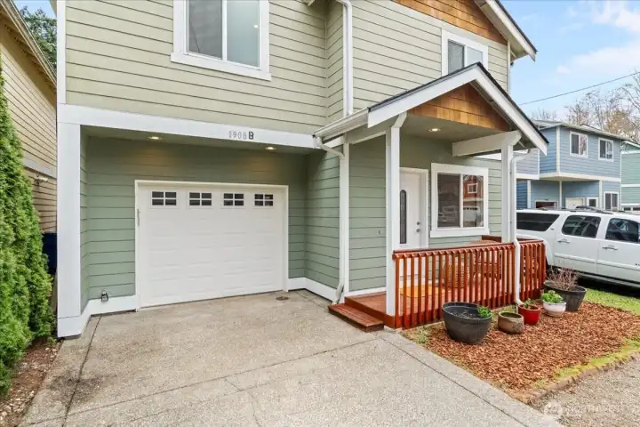 Covered front porch with wood railing creates a welcoming entry. Attached single-car garage and concrete driveway provide convenient off-street parking.