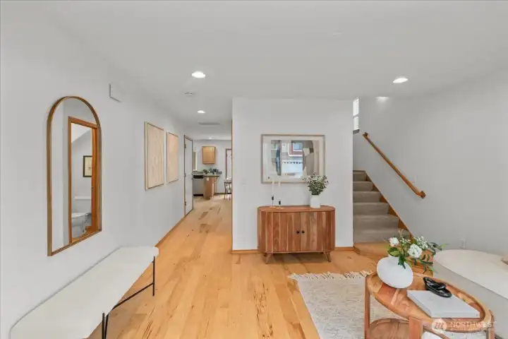 Front living area with laminate flooring and recessed lighting, positioned near the entry and staircase. The space flows toward the kitchen and dining area for easy everyday living.