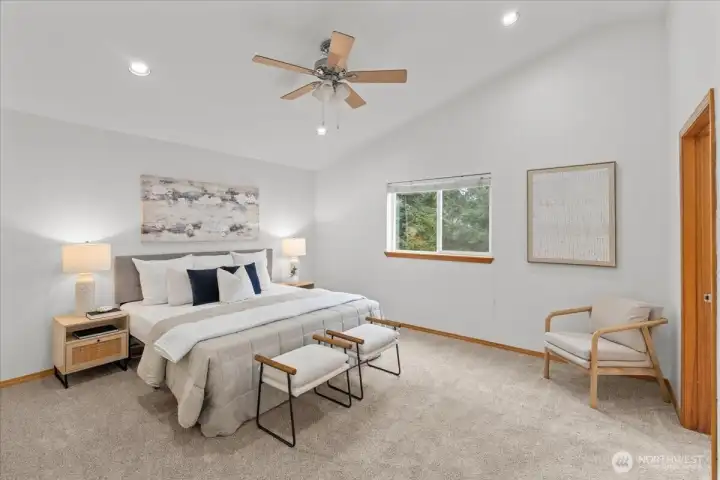 Spacious primary bedroom with high ceiling, ceiling fan, and large window for natural light. Carpeted flooring and neutral finishes create a comfortable retreat.