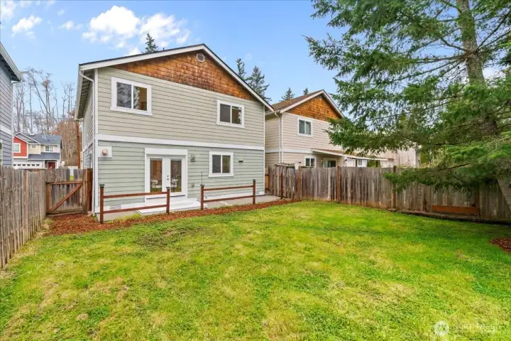 Rear exterior view of the home featuring double glass doors leading to the backyard. Fenced yard and surrounding trees create a private outdoor setting.