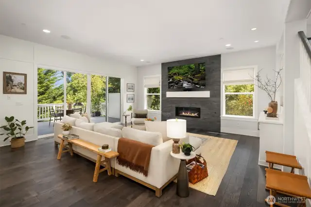 The heart of the main floor showcases a chef-inspired kitchen with an oversized white island and premium appliance suite, flowing effortlessly to a covered outdoor entertaining deck with inviting fireplace.