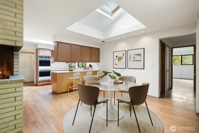 Kitchen eating space with large skylight, hardwood floors, fireplace and open kitchen - views to large bedroom down the hall to the right. Virtually staged to show potential of this space!