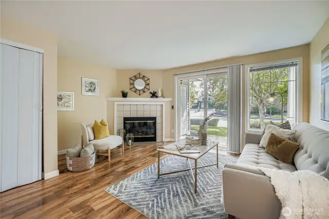 Bright and inviting living room features a cozy wood-burning fireplace, perfect for relaxing evenings. Freshly painted walls and beautiful laminate flooring create a warm, modern feel. Large windows and sliding glass doors flood the space with natural light and provide easy access to the patio—ideal for indoor-outdoor living.