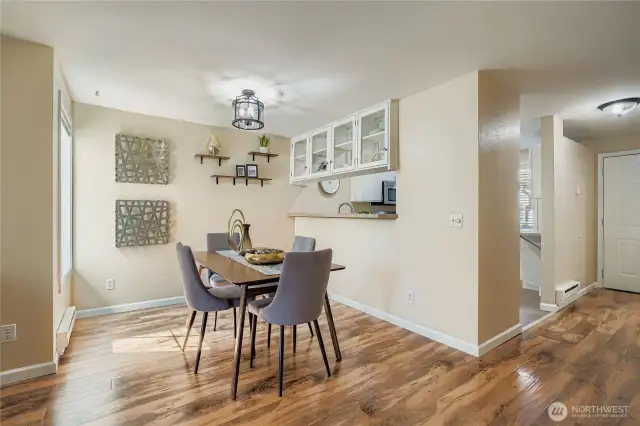 Charming dining area bathed in natural light from a large picture window, creating a warm and inviting space for meals. Elegant laminate flooring flows seamlessly throughout, while the open pass-through to the kitchen adds convenience and connection for entertaining.