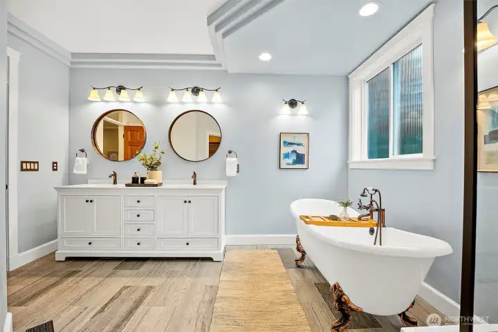 Primary en-suite bathroom facing double-sink farmhouse vanity with clawfoot soaking tub.