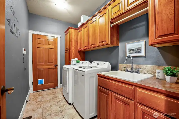 Utility room featuring lots of storage cabinets, cat door to garage and utility sink with countertop space.