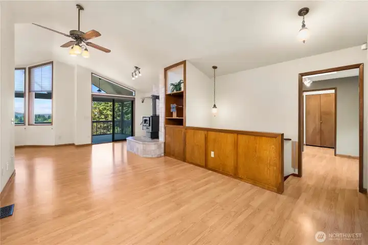 The stairway to downstairs tucked behind the wood trimmed half wall and the sliding doors out to the deck just past the wood stove. High ceilings.