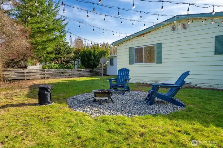 Backyard seating area under café lights with a propane fire pit creates a charming space for cozy evenings and outdoor gatherings.