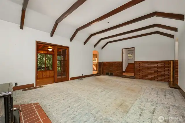 Open living room large enough for large gatherings, with timber framed ceilings, unique wooden brick, and cozy wood stove.