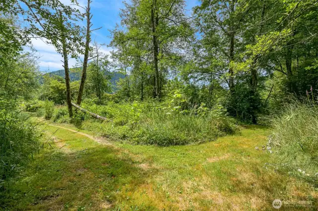 Extra wide groomed trail system throughout, seen here, leading to the lower pasture, outbuilding, greenhouse frame, power meter and incredible pond.