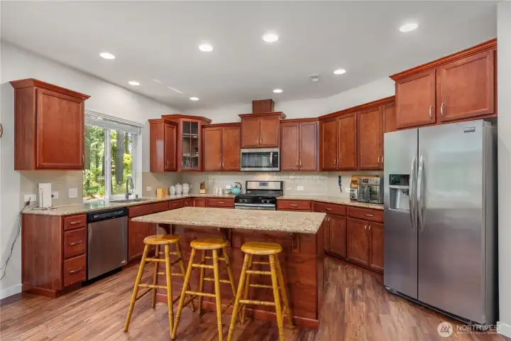 Spacious kitchen with granite island, rich wood cabinetry, stainless appliances, gas range, tile backsplash, and abundant cabinet storage. Spacious kitchen with granite island, rich wood cabinetry, stainless appliances, gas range, tile backsplash, and abundant cabinet storage.