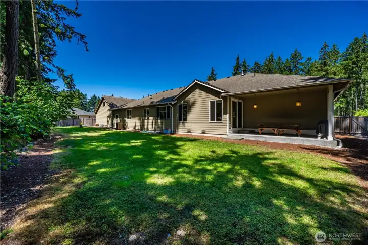 Rear exterior view of the spacious rambler featuring a covered patio, level backyard, mature evergreens, and peaceful outdoor privacy. Rear exterior view of the spacious rambler featuring a covered patio, level backyard, mature evergreens, and peaceful outdoor privacy.