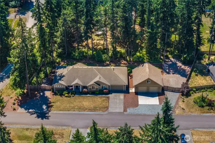 Overhead aerial view showcasing the home, detached shop, driveway layout, front lawn, gravel parking, and tree-lined property setting. Overhead aerial view showcasing the home, detached shop, driveway layout, front lawn, gravel parking, and tree-lined property setting.