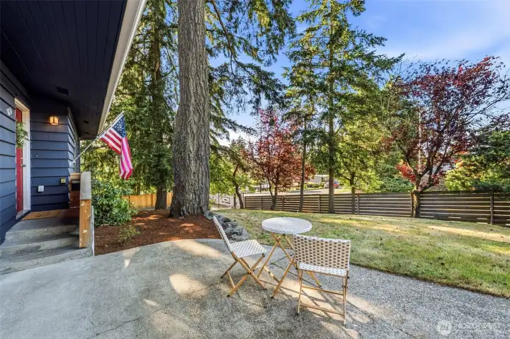 Poured concrete patio for  the front yard surrounded by mature landscaping and a fully fenced lot.