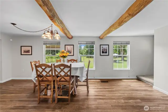 This bright and spacious dining room features large picture windows that frame serene views of the private acreage, flooding the space with natural light. With real hardwood floors, rustic exposed log ceiling beams, and a central chandelier, this room blends Pacific Northwest charm with modern comfort. Perfect for hosting, this open-concept layout flows seamlessly into the kitchen and living areas, offering both warmth and functionality for everyday living or entertaining. Ideal for buyers seeking a country home with acreage, a move-in ready farmhouse, or a rural property in Washington State.
