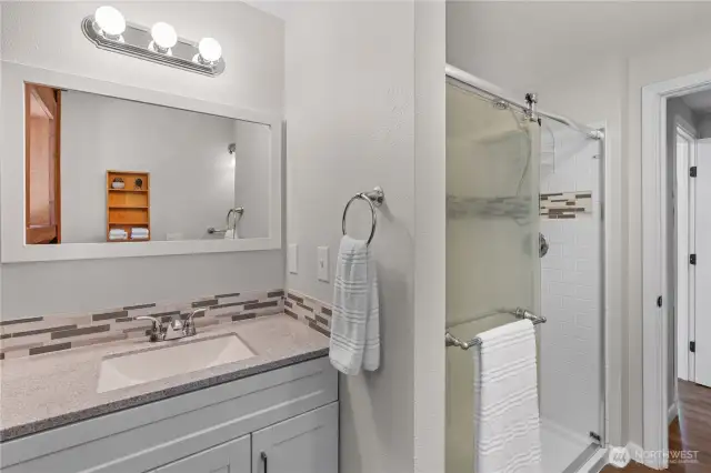Modern Bathroom with Custom Tile & Walk-In Shower  This beautifully updated bathroom features a sleek vanity with stone-style countertops, mosaic tile backsplash & a large framed mirror for a bright, clean look. The spacious walk-in shower is finished with contemporary subway tile & a coordinating accent stripe, blending style & function. With neutral tones & quality finishes, this space offers a relaxing retreat for daily routines—perfect for buyers seeking move-in-ready comfort with modern updates.